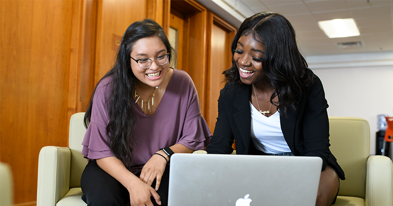 two women looking at their laptop on table