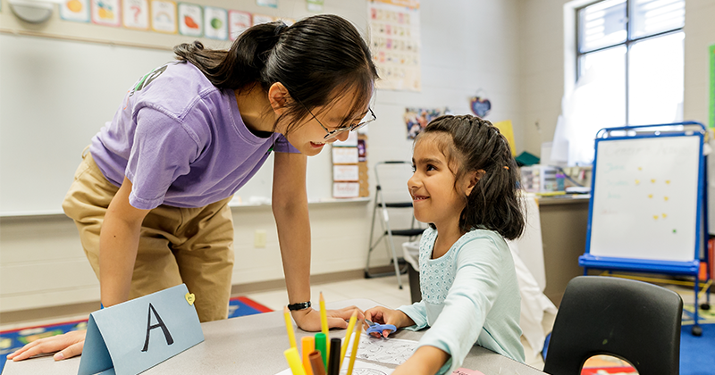 teacher leaning over table with student