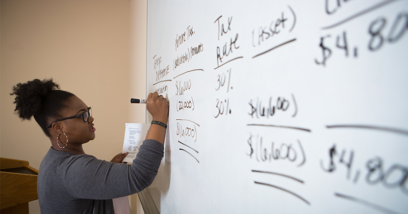 masters in accountancy teacher at whiteboard doing calculations