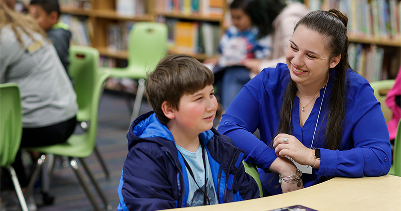 teacher at desk with boy in library