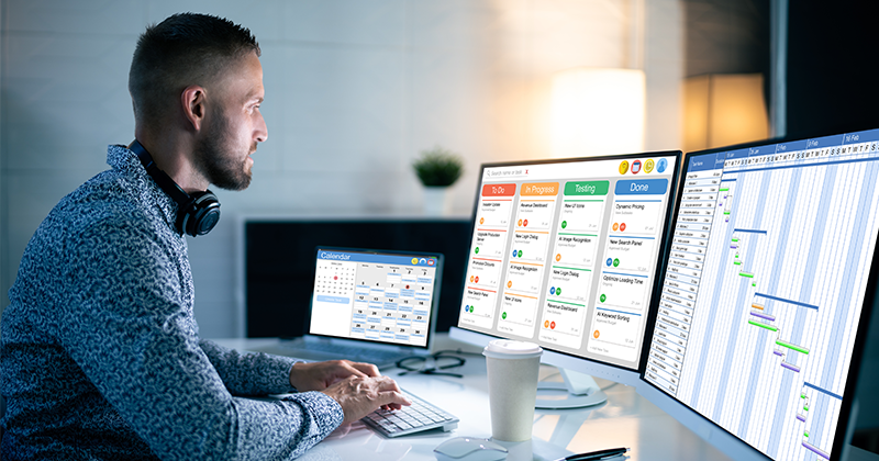 project manager at desk with multiple monitors