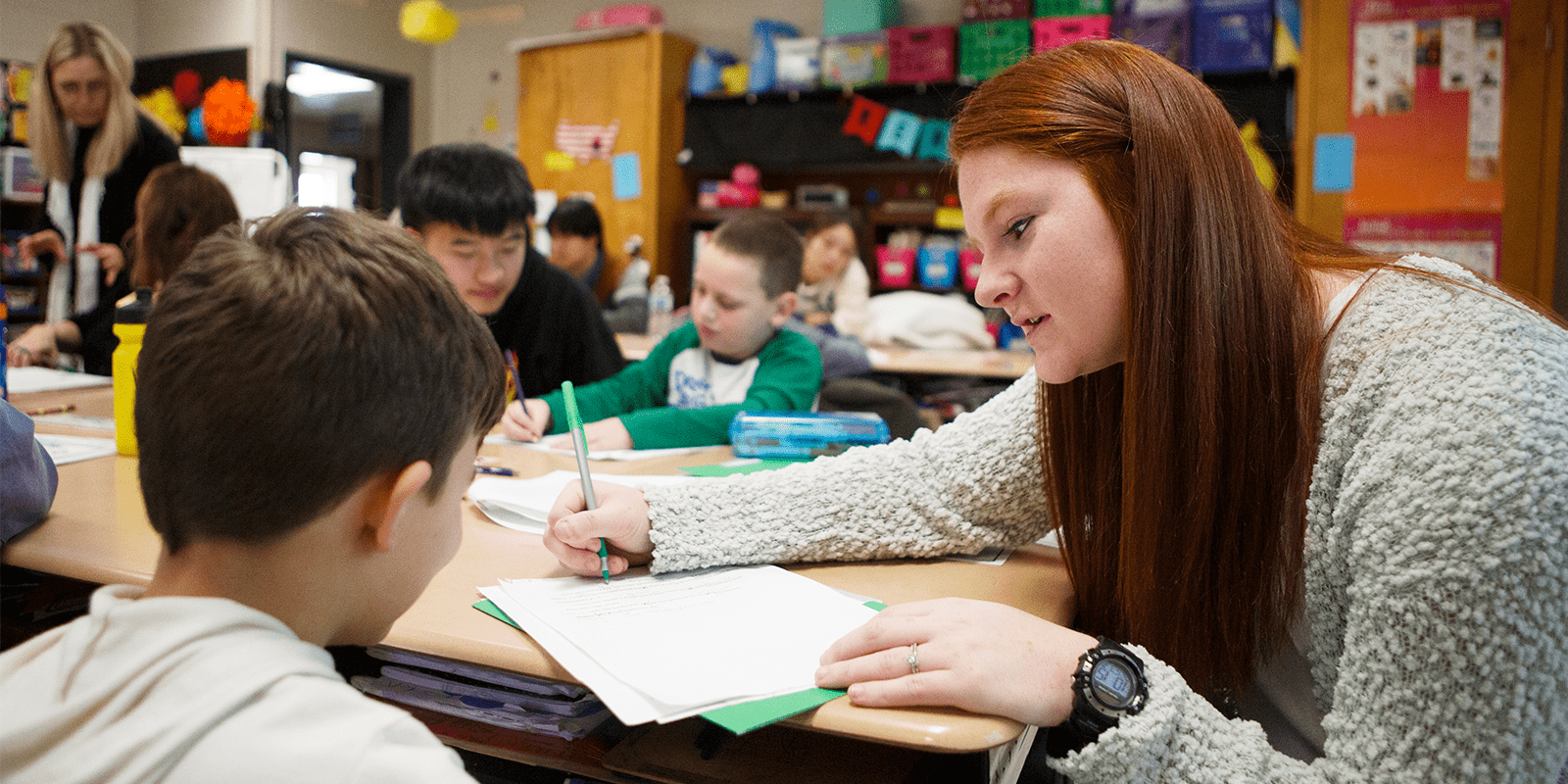 red haired teacher with bachelor in special education at table with students in classroom