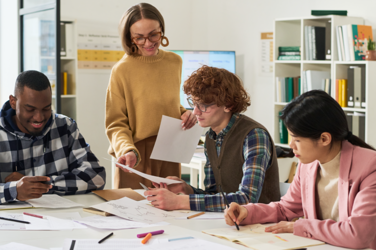 Teacher helping diverse students review papers at classroom table