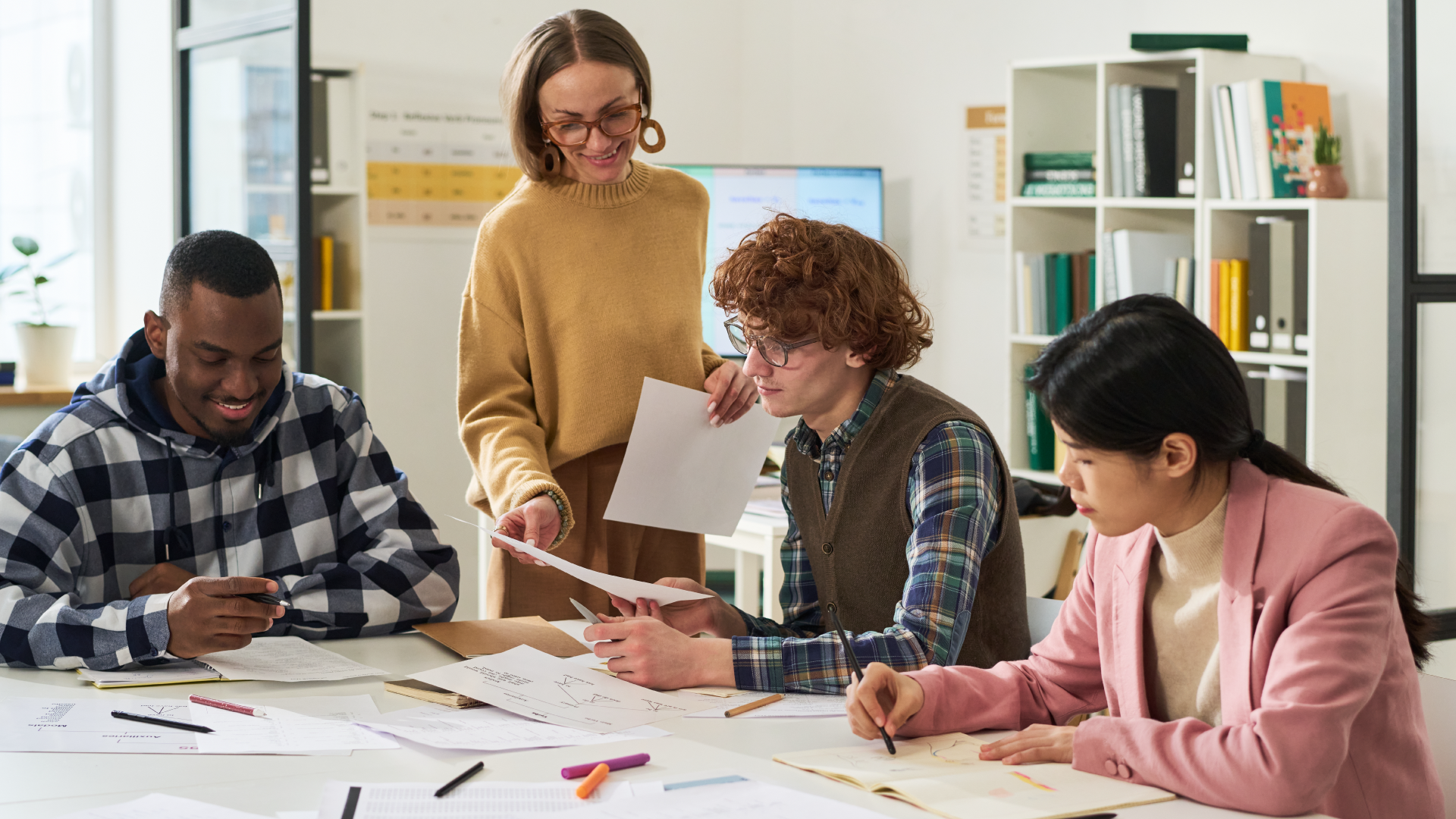 Teacher helping diverse students review papers at classroom table
