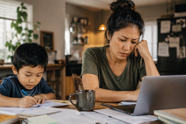 Stressed mother helping son with homework while working on laptop