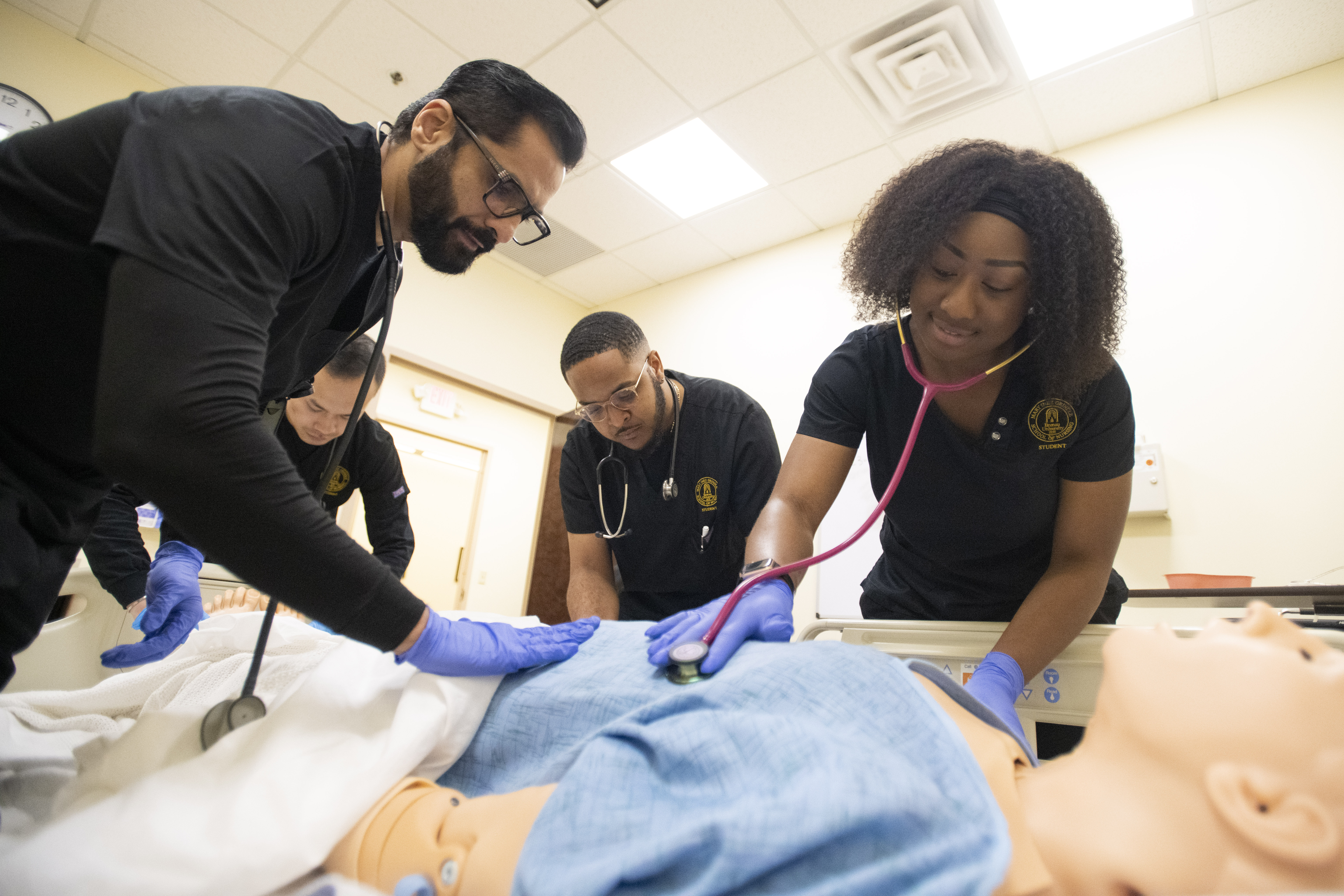 Nursing students practice patient assessment with stethoscope on medical simulation mannequin