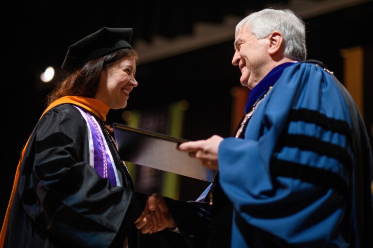 Graduate in doctoral regalia shaking hands with university president on stage